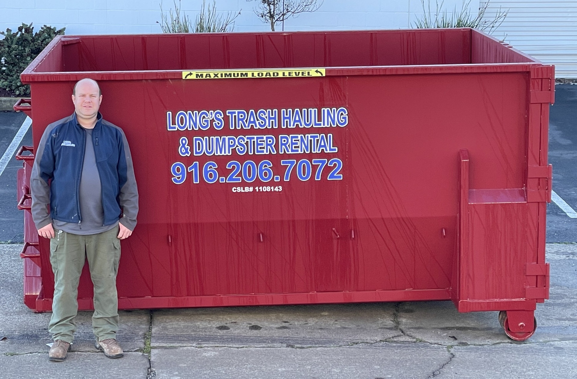 Jim Long standing next to a Long's Trash Hauling red roll-off dumpster