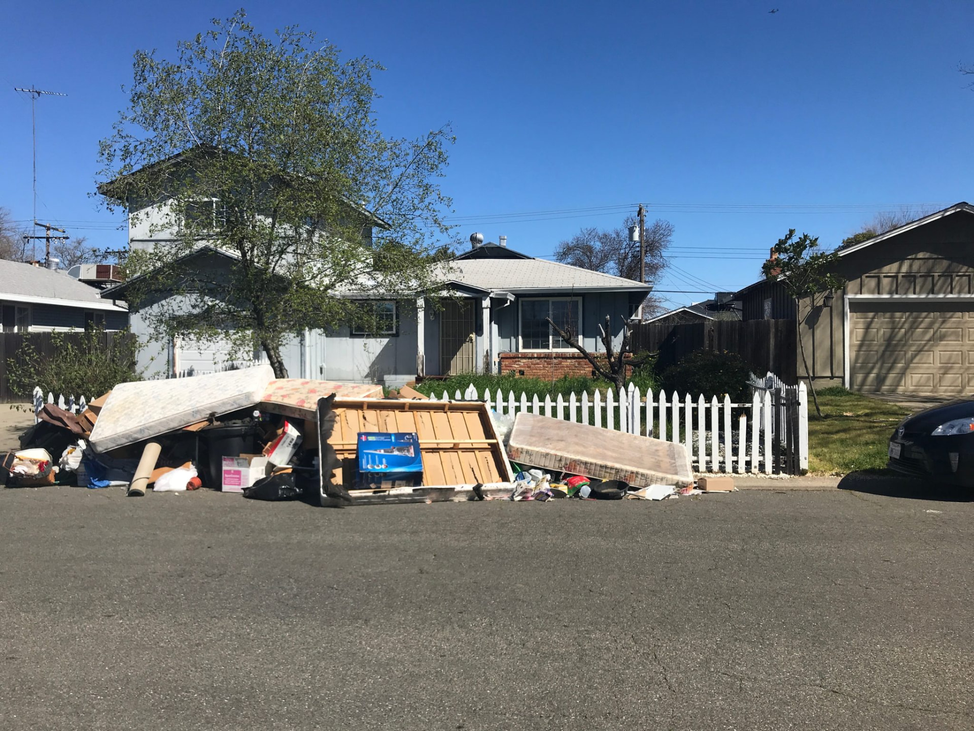 Mattresses, furniture, and bagged household junk piled at the curb in front of a Sacramento home